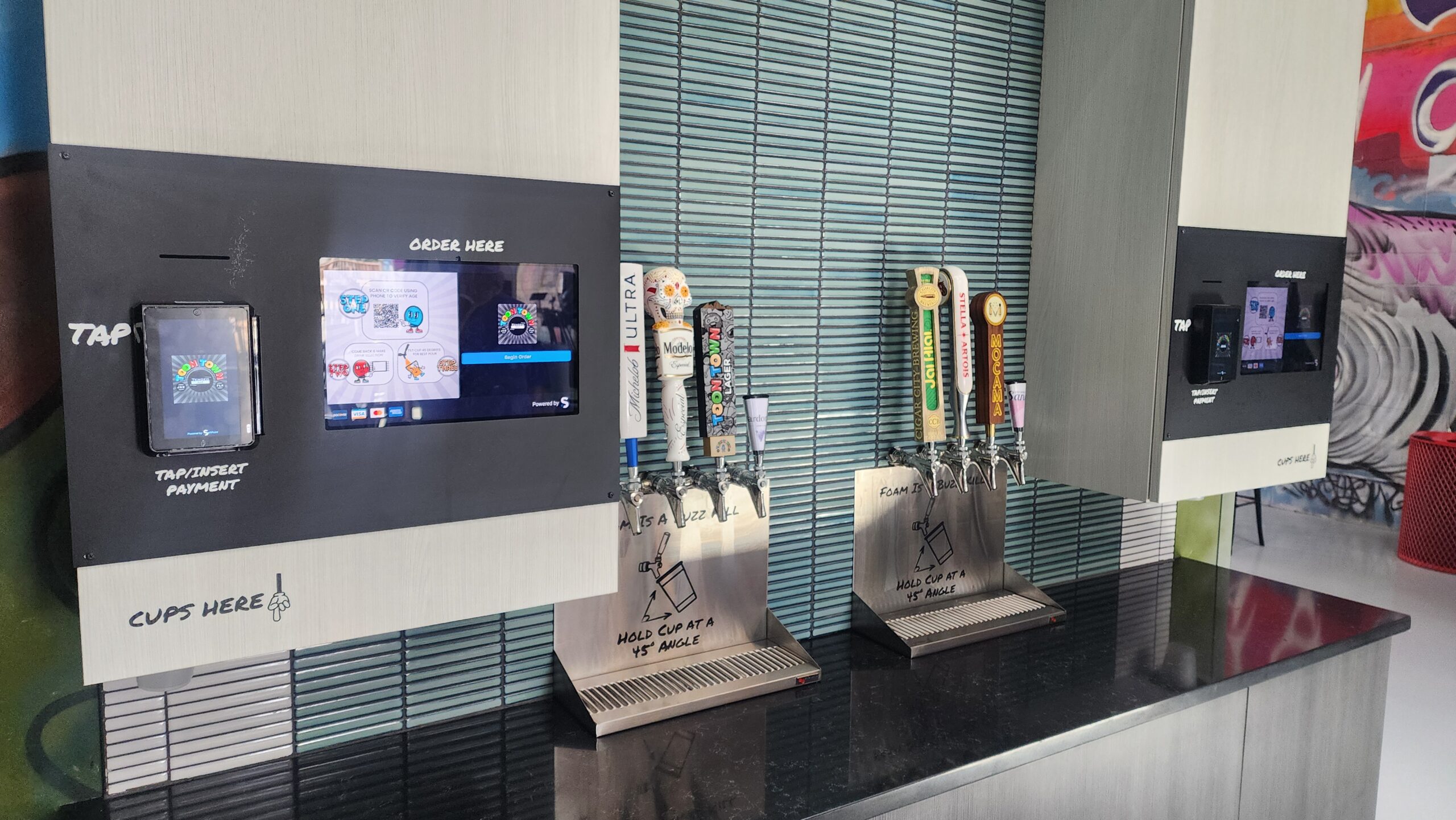 Unattended TendedBar vending wall with order-here screen, tap handles, and cups-here signage, no attendant